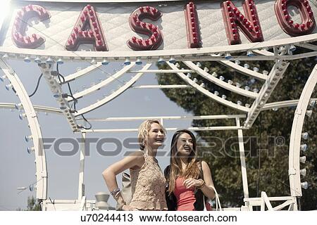 Stock Image - Two women standing in front of fairground ride, laughing. Fotosearch