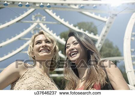 Stock Photo - Two women standing in front of fairground ride, laughing. Fotosearch