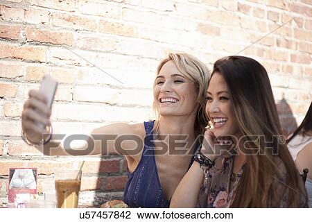 Stock Image - Two women, taking self portrait at restaurant. Fotosearch