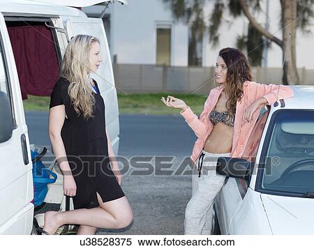 Two young women leaning on cars gossiping on street View Large Photo Image Stock Photography - Two young women leaning on cars gossiping on street. Fotosearch