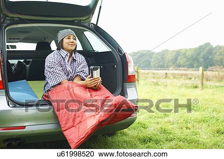 Woman sitting at rear of car with legs tucked in sleeping bag View Large Photo Image Stock Image - Woman sitting at rear of car with legs tucked in sleeping bag. Fotosearch