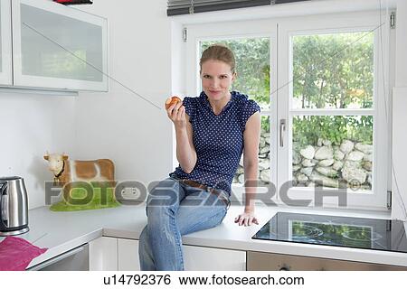 Woman sitting on kitchen counter eating apple View Large Photo Image Stock Photograph - Woman sitting on kitchen counter eating apple. Fotosearch