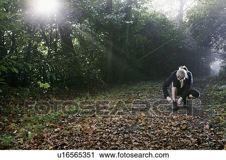 Stock Image - Woman tying shoelace in woods. Fotosearch