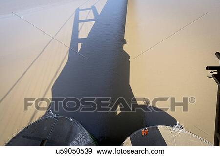 Stock Photo - Workers standing in the shadow of suspension bridge. The Humber Bridge, UK was built in 1981 and at the time was the world's largest single-span suspension bridge. Fotosearch