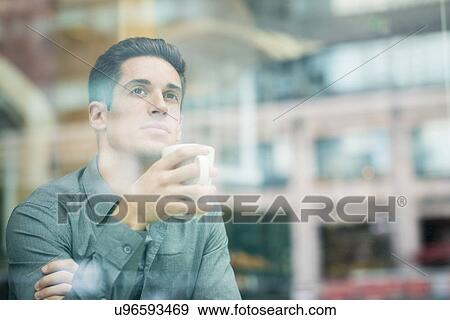 Young businessman drinking coffee and looking out of cafe window, London, UK View Large Photo Image Stock Photo - Young businessman drinking coffee and looking out of cafe window, London, UK. Fotosearch