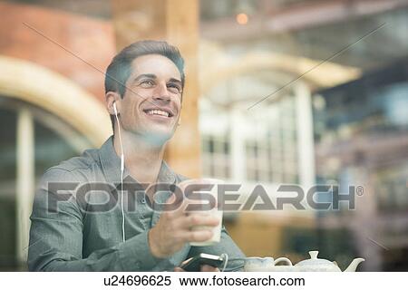 Young businessman listening to earphones in cafe window seat, London, UK View Large Photo Image Stock Photography - Young businessman listening to earphones in cafe window seat, London, UK. Fotosearch