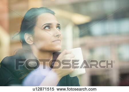 Stock Photography - Young businesswoman drinking coffee and looking out of cafe window, London, UK. Fotosearch
