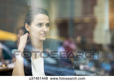Stock Photo - Young businesswoman looking out of cafe window, London, UK. Fotosearch