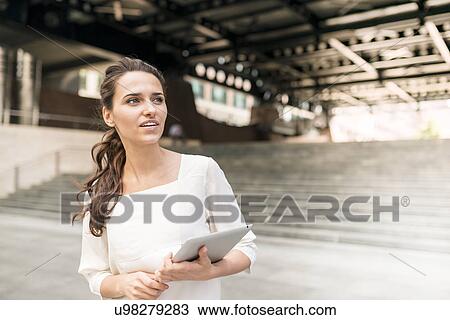 Stock Image - Young businesswoman waiting outside station with digital tablet, London, UK. Fotosearch