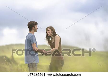 Young couple holding hands together in meadow under bright sky View Large Photo Image Stock Image - Young couple holding hands together in meadow under bright sky. Fotosearch