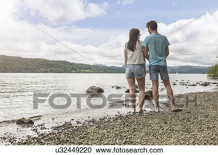 Young couple looking to each other at the edge of lake under sunny sky View Large Photo Image Stock Image - Young couple looking to each other at the edge of lake under sunny sky. Fotosearch