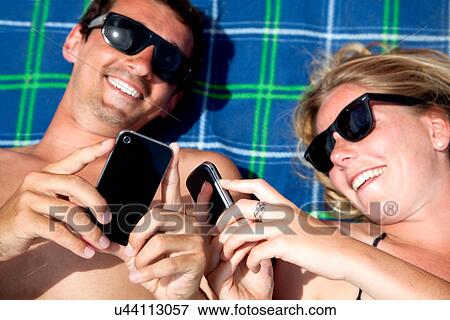 Young couple lying on beach towel using smartphones View Large Photo Image Stock Photo - Young couple lying on beach towel using smartphones. Fotosearch