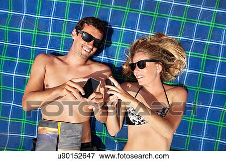 Young couple lying on beach towel using smartphones View Large Photo Image Stock Photo - Young couple lying on beach towel using smartphones. Fotosearch