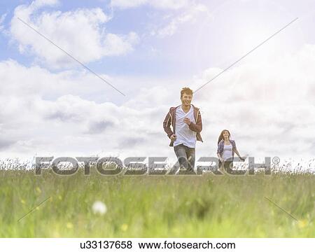 Stock Photo - Young couple running through meadow under bright sunshine. Fotosearch