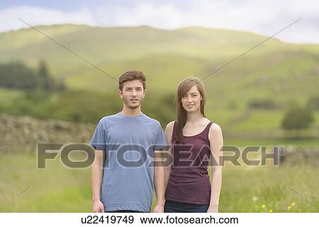 Stock Photo - Young couple standing together in meadow and looking away over rural landscape. Fotosearch