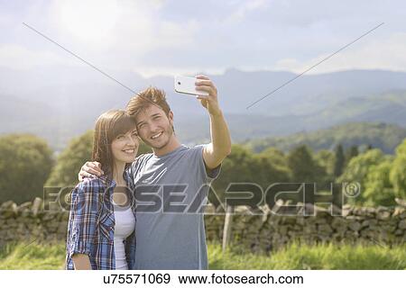 Young couple taking self portrait on mobile phone in countryside under sunny sky View Large Photo Image Stock Photo - Young couple taking self portrait on mobile phone in countryside under sunny sky. Fotosearch