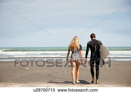 Young couple walking out to sea, young man carrying surfboard View Large Photo Image Stock Photography - Young couple walking out to sea, young man carrying surfboard. Fotosearch