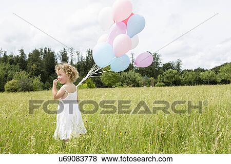 Stock Photo - Young girl holding balloons in field. Fotosearch
