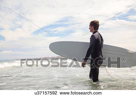 Young man carrying surfboard, walking out to sea View Large Photo Image Stock Image - Young man carrying surfboard, walking out to sea. Fotosearch