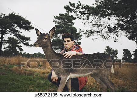 Young man crouching in field petting a deer View Large Photo Image Stock Photography - Young man crouching in field petting a deer. Fotosearch