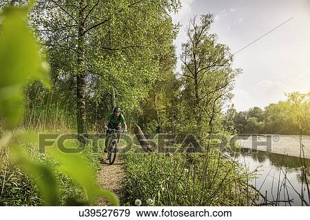 Stock Photo - Young man cycling along riverside path. Fotosearch