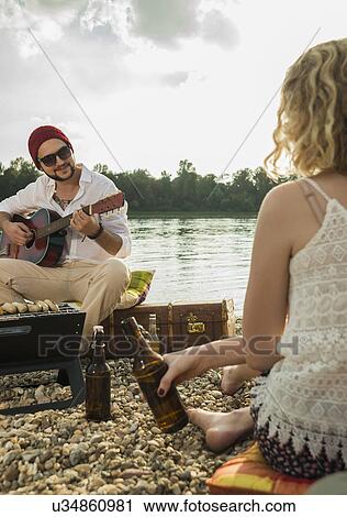 Young man sitting by lake playing guitar View Large Photo Image Stock Image - Young man sitting by lake playing guitar. Fotosearch