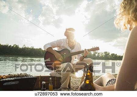 Young man sitting by lake playing guitar View Large Photo Image Stock Image - Young man sitting by lake playing guitar. Fotosearch
