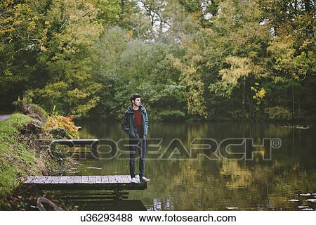 Stock Photo - Young man standing on edge of river pier. Fotosearch