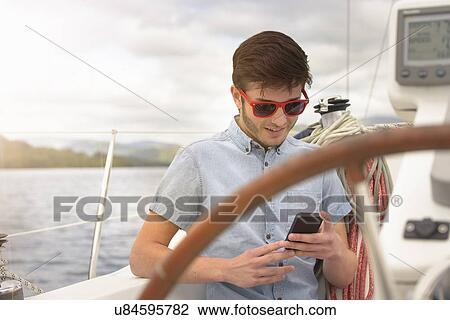 Young man using mobile phone on yacht under sunny sky View Large Photo Image Stock Image - Young man using mobile phone on yacht under sunny sky. Fotosearch