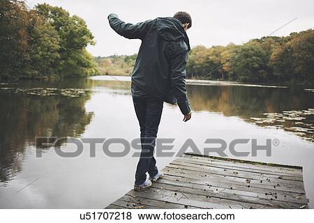 Stock Photo - Young man walking along edge of river pier. Fotosearch