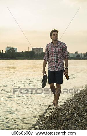 Young man walking by lake carrying shoes View Large Photo Image Stock Photo - Young man walking by lake carrying shoes. Fotosearch