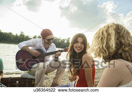 Stock Image - Young man with friends playing guitar. Fotosearch