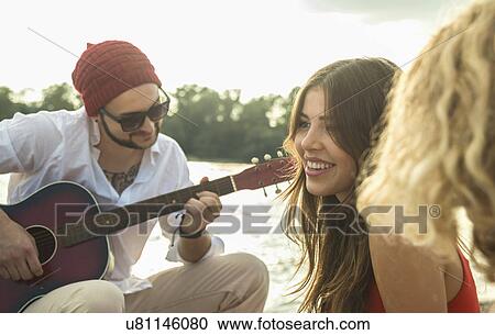 Stock Image - Young man with friends playing guitar. Fotosearch