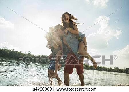 Stock Image - Young men giving young women piggy backs. Fotosearch