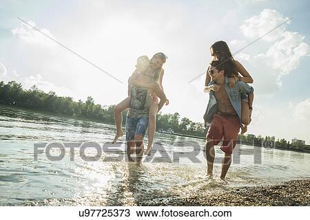 Stock Image - Young men giving young women piggy backs. Fotosearch