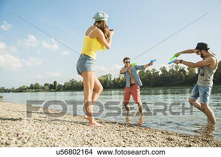 Young men playing with water pistols in lake View Large Photo Image Picture - Young men playing with water pistols in lake. Fotosearch
