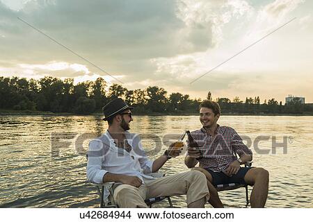 Young men toasting with beer bottles by lake View Large Photo Image Picture - Young men toasting with beer bottles by lake. Fotosearch