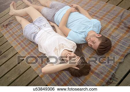 Stock Photograph - Young smiling couple lying on blanket on jetty. Fotosearch