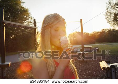 Young woman eating ice cream cone in park at sunset View Large Photo Image Picture - Young woman eating ice cream cone in park at sunset. Fotosearch
