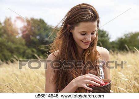 Stock Photograph - Young woman holding bowl of fresh fruit in field. Fotosearch