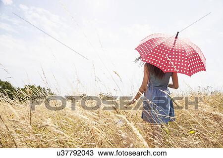 Stock Image - Young woman in field with umbrella. Fotosearch
