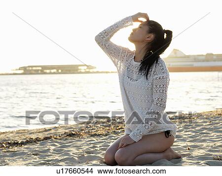 Picture - Young woman kneeling on sunlit beach, Port Melbourne, Melbourne, Victoria, Australia. Fotosearch