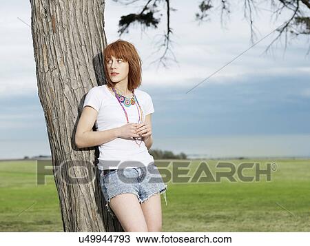 Stock Image - Young woman leaning against tree, Williamstown beach, Melbourne, Australia. Fotosearch