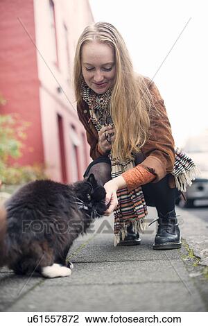 Young woman petting black cat on pavement View Large Photo Image Stock Image - Young woman petting black cat on pavement. Fotosearch