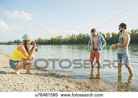 Young woman photographing men by lake View Large Photo Image Stock Photography - Young woman photographing men by lake. Fotosearch