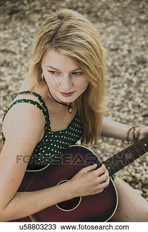 Stock Image - Young woman playing guitar, high angle. Fotosearch
