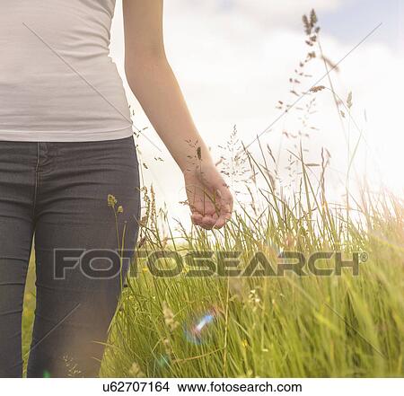 Picture - Young woman running hand through long grass in meadow under bright sunshine, close up. Fotosearch