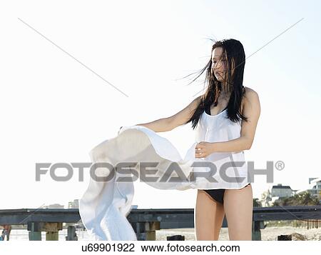 Stock Image - Young woman shaking beach towel on beach, Port Melbourne, Melbourne, Victoria, Australia. Fotosearch