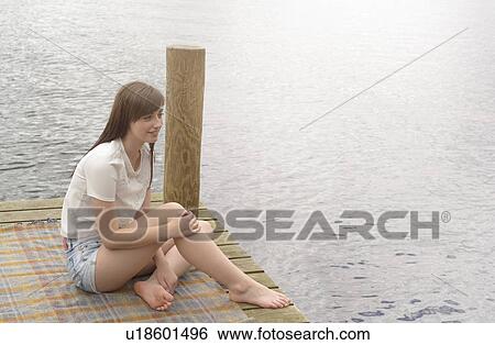 Young woman sitting at the end of a lakeside jetty View Large Photo Image Stock Photograph - Young woman sitting at the end of a lakeside jetty. Fotosearch