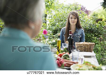 Stock Image - Young woman sitting down for meal in garden. Fotosearch